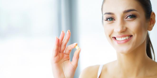 Woman with glowing healthy skin about to take her fish oil supplement